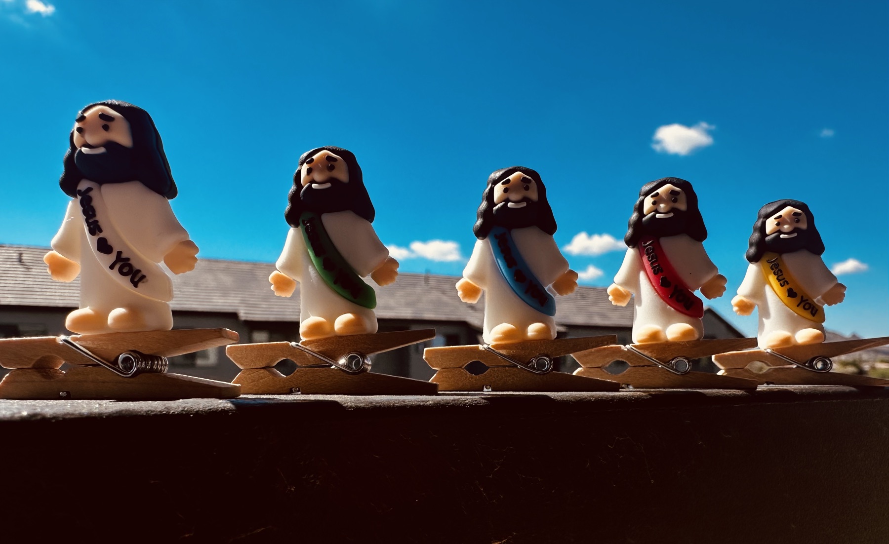 Five Clip On Jesus figures lined up on wooden clothespins against a bright blue Arizona sky